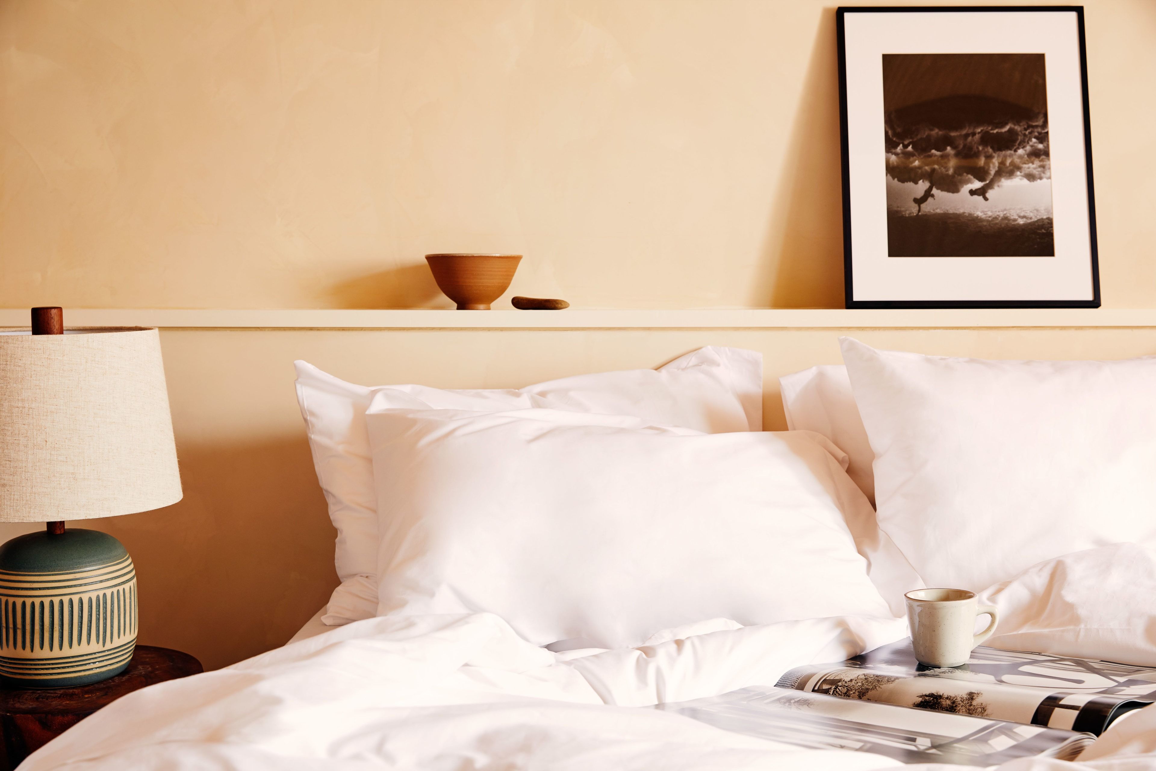 A bed with a coffee, pillows, a magazine